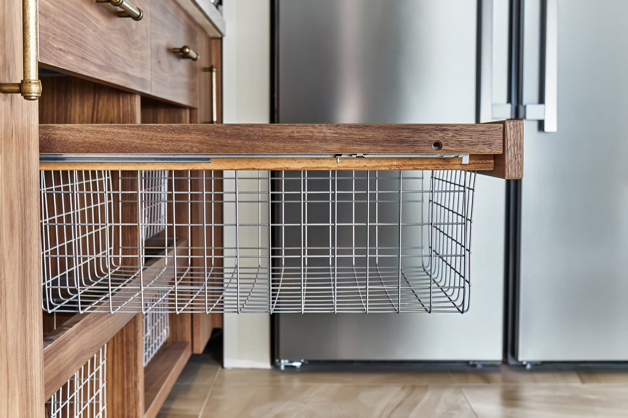 Stainless steel wire basket pulled out of a kitchen base cabinet