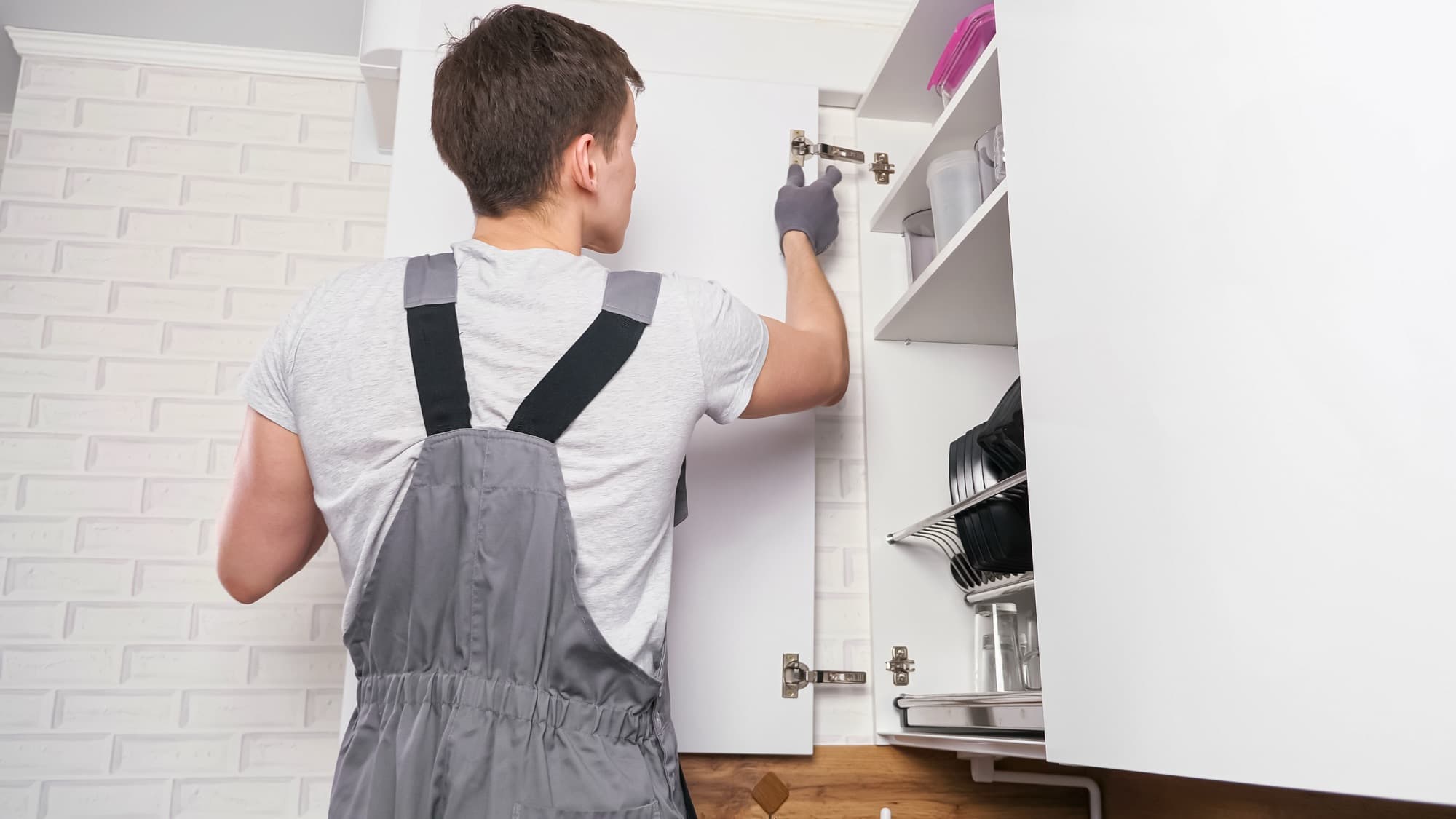 Technician adjusting the hinge of a kitchen wall cabinet door