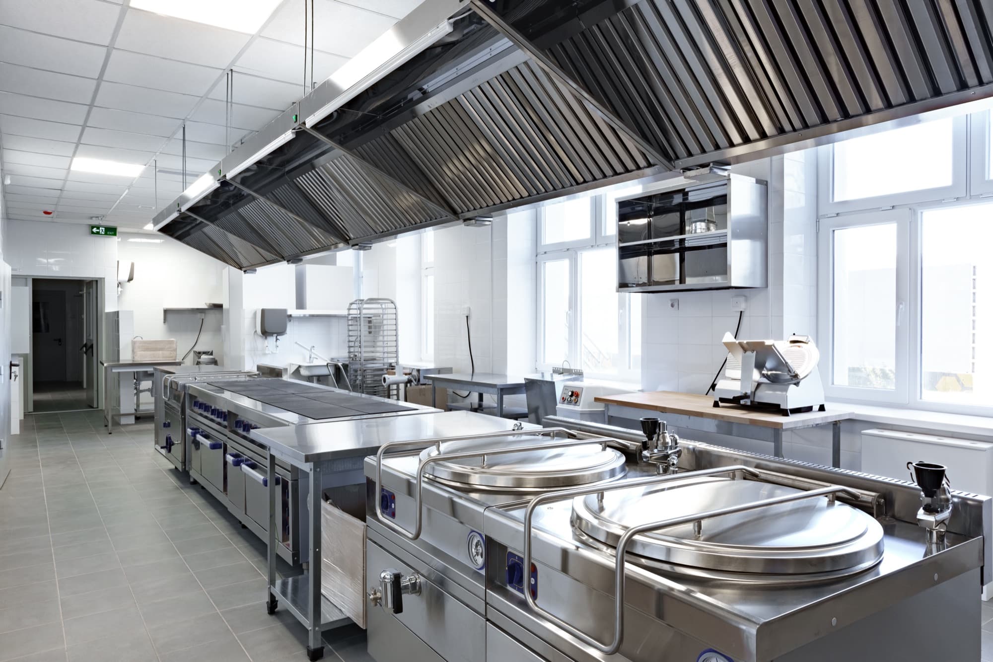 Bright commercial kitchen with stainless steel tables and exhaust hoods